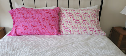 Two handmade pillowcases in coordinating pink and red prints, propped upright against a black metal bedframe.