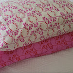 Two handmade pillowcases in coordinating pink and red prints, displayed on a white quilted bed.