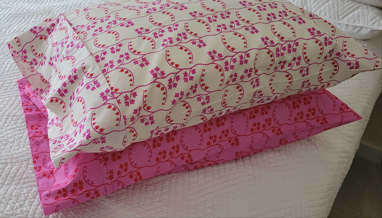Two handmade pillowcases in coordinating pink and red prints, displayed on a white quilted bed.