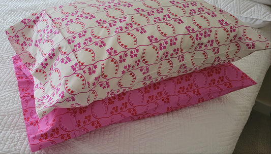 Two handmade pillowcases in coordinating pink and red prints, displayed on a white quilted bed.