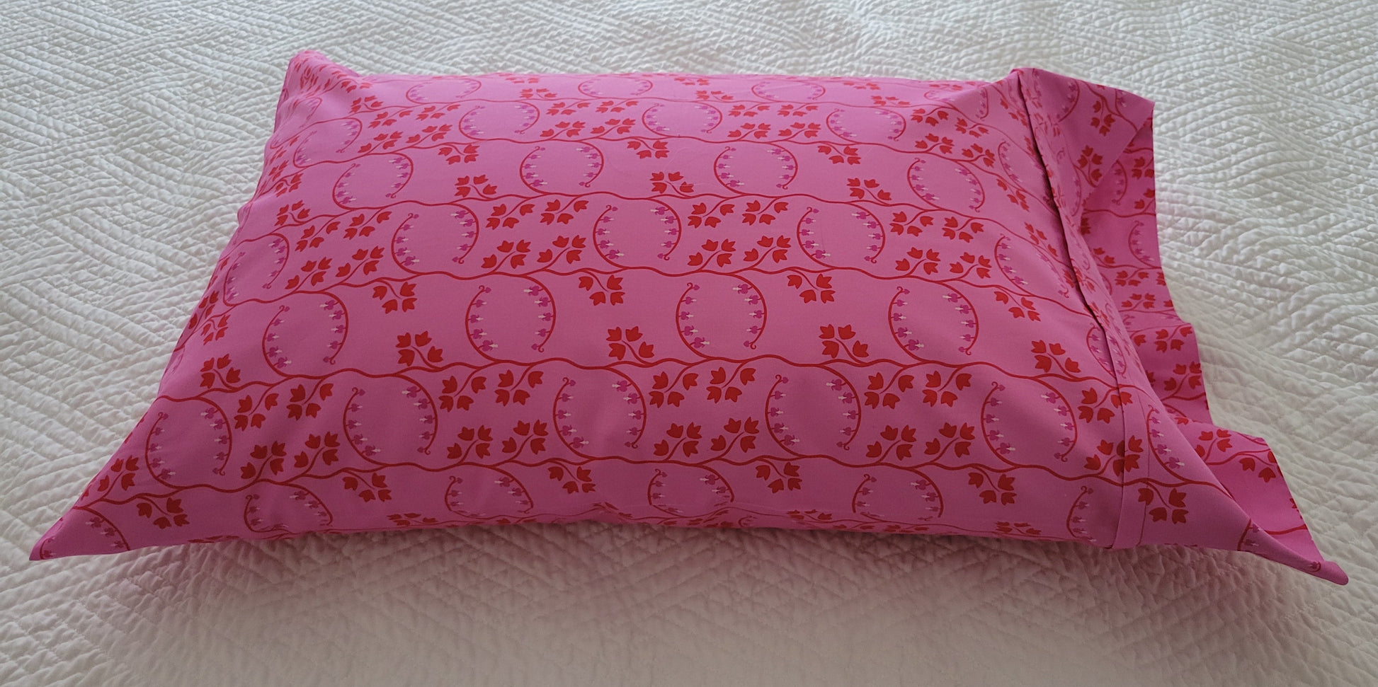Handmade pink pillowcase with a red floral print, displayed on a white quilted bed.