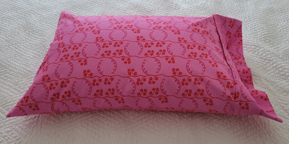 Handmade pink pillowcase with a red floral print, displayed on a white quilted bed.