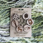 Set of six engraved wooden Pacific Northwest stitch markers displayed on a Sunrise Grove Knittery backing card.