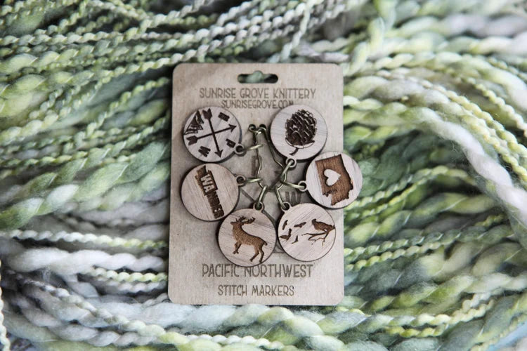 Set of six engraved wooden Pacific Northwest stitch markers displayed on a Sunrise Grove Knittery backing card.