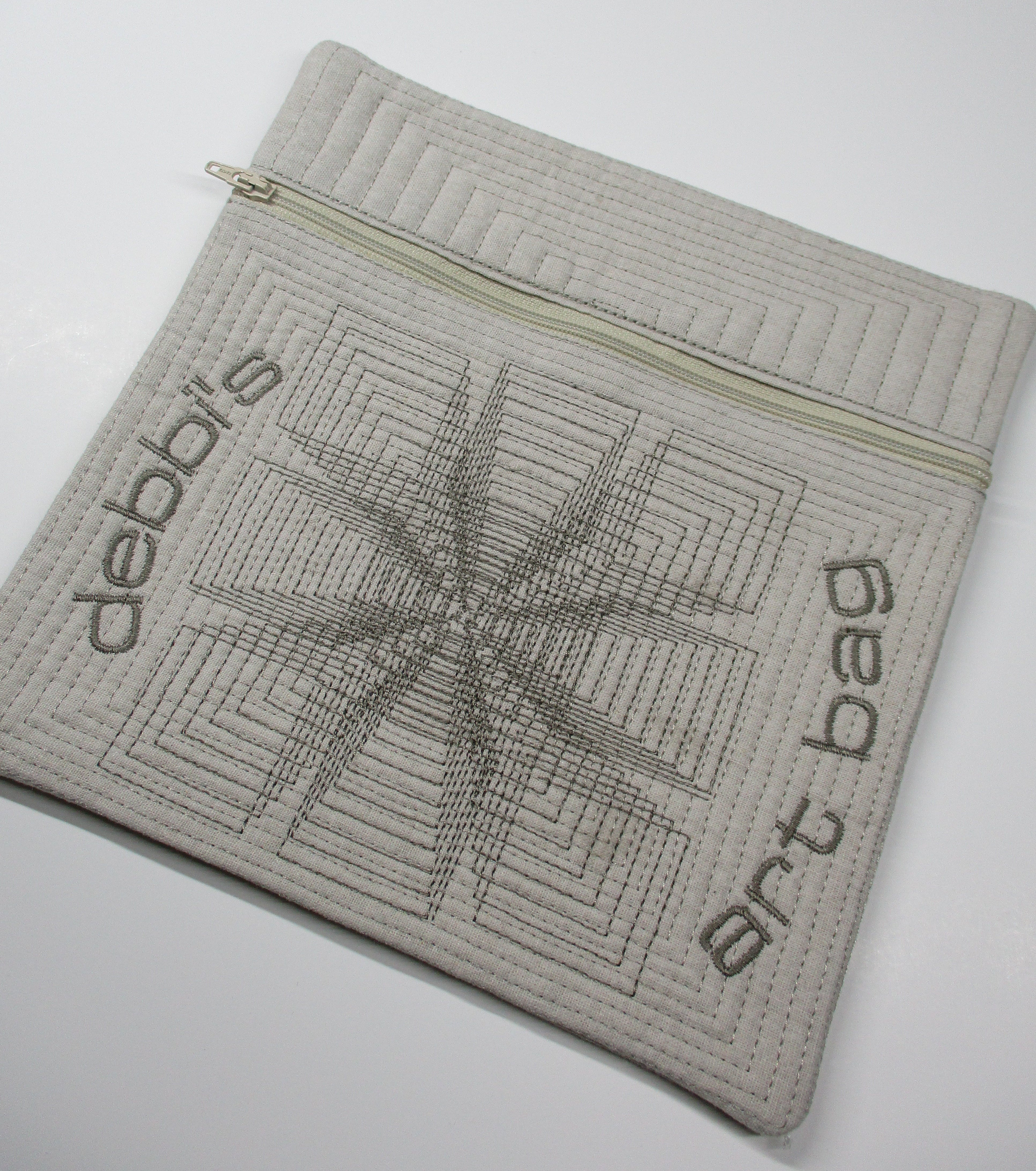 Quilted zippered pouch with geometric stitching and embroidered ‘debbi’s art bag’ lettering