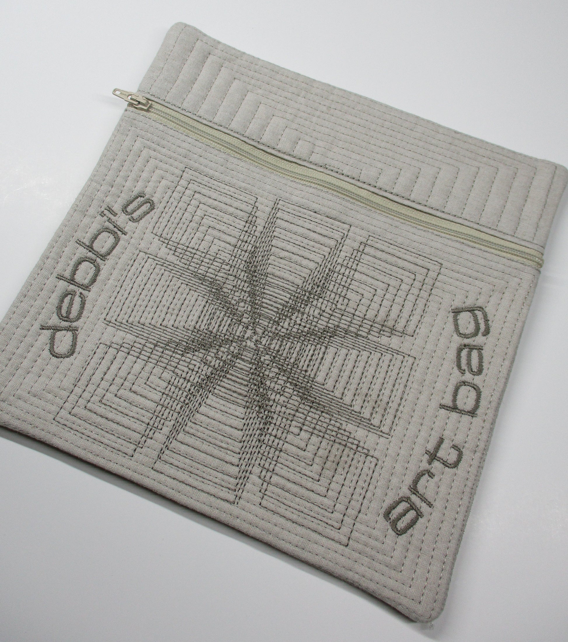 Quilted zippered pouch with geometric stitching and embroidered ‘debbi’s art bag’ lettering