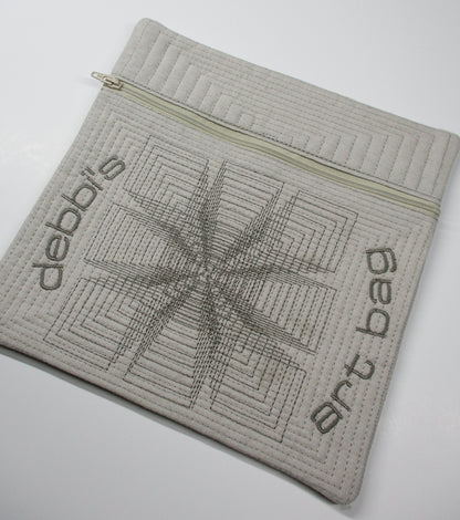 Quilted zippered pouch with geometric stitching and embroidered ‘debbi’s art bag’ lettering