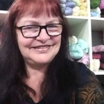 Instructor Teresa Wilson smiling in front of shelves filled with colorful yarn.