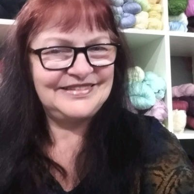 Instructor Teresa Wilson smiling in front of shelves filled with colorful yarn.