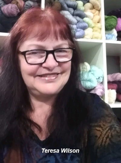 Instructor Teresa Wilson smiling in front of shelves filled with colorful yarn.