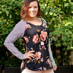 Outdoor view of the Rio Raglan with long striped sleeves and a floral front panel, worn with shorts against a leafy garden backdrop