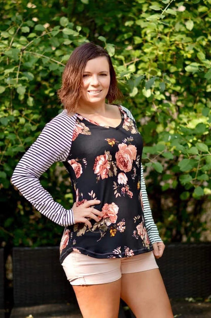 Outdoor view of the Rio Raglan with long striped sleeves and a floral front panel, worn with shorts against a leafy garden backdrop