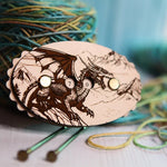 Wooden dragon‑engraved row counter with number dials, shown beside multicolored yarn and knitting needles.