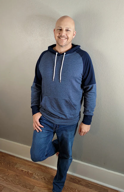 Indoor view of the Santa Fe Hoodie sewn as a pullover with a hood, featuring blue and navy color‑blocking and white drawstrings, worn with jeans against a light wall