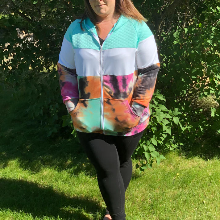 Outdoor view of the Santa Fe Hoodie sewn as a full‑zip hoodie in a colorful tie‑dye print, worn with black leggings in a grassy setting