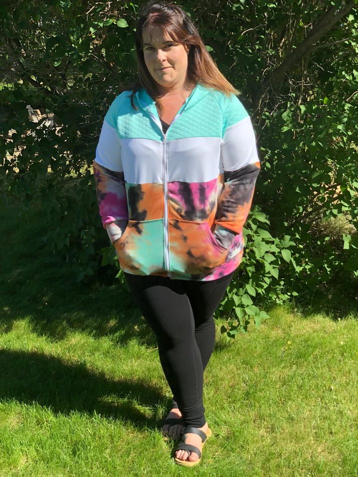 Outdoor view of the Santa Fe Hoodie sewn as a full‑zip hoodie in a colorful tie‑dye print, worn with black leggings in a grassy setting