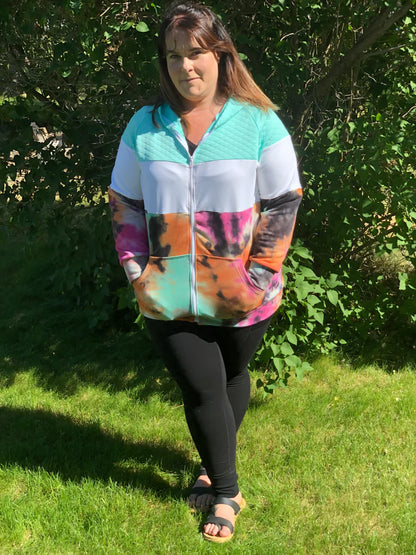 Outdoor view of the Santa Fe Hoodie sewn as a full‑zip hoodie in a colorful tie‑dye print, worn with black leggings in a grassy setting