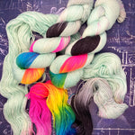 Pale mint hand‑dyed yarn with bright rainbow and black sections arranged on a dark schematic background.