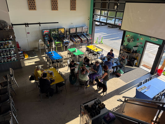 View from above of the entry level at Barley Pop, with Mindy standing beside her dog Jasper while people gather at tables for Stitch ’n Bitch.