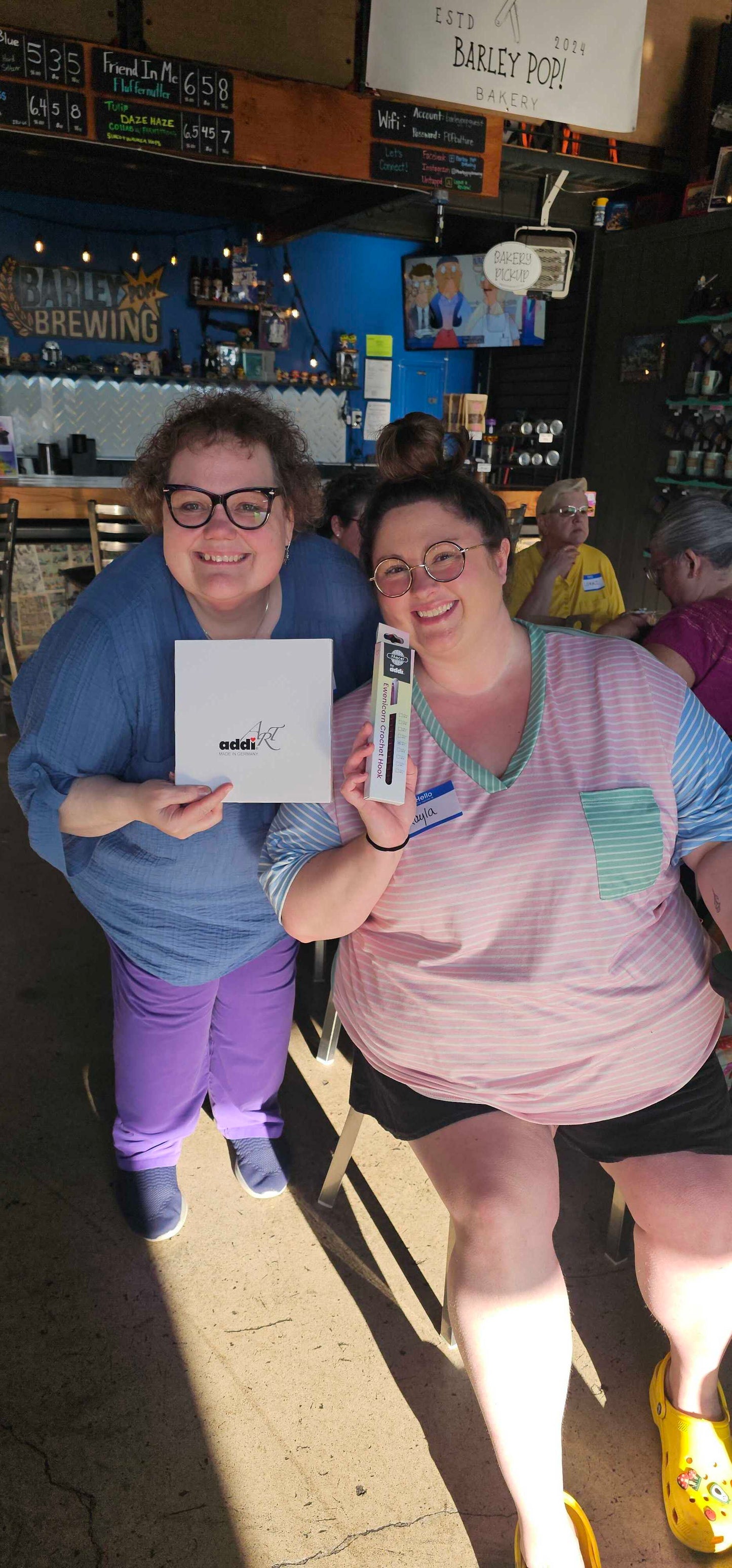 Two Stitch ’n Bitch prize winners at Barley Pop Brewing holding Skacel knitting and crochet tools and smiling during the event.