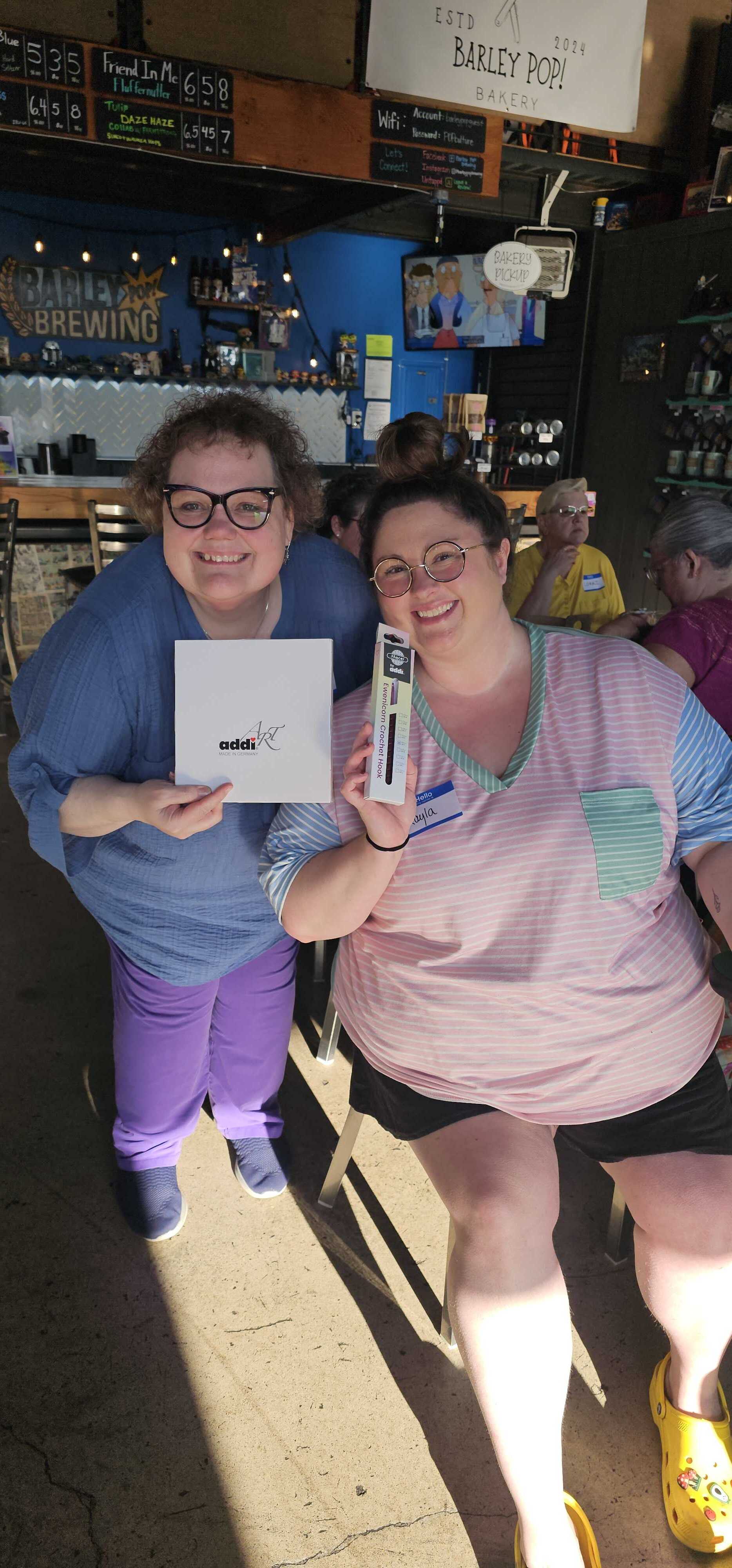 Two Stitch ’n Bitch prize winners at Barley Pop Brewing holding Skacel knitting and crochet tools and smiling during the event.