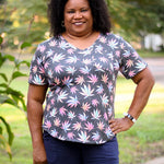 Outdoor view of the Sulky Perfect Tee sewn in a dark knit with a colorful leaf print, paired with dark shorts on a tree‑lined path