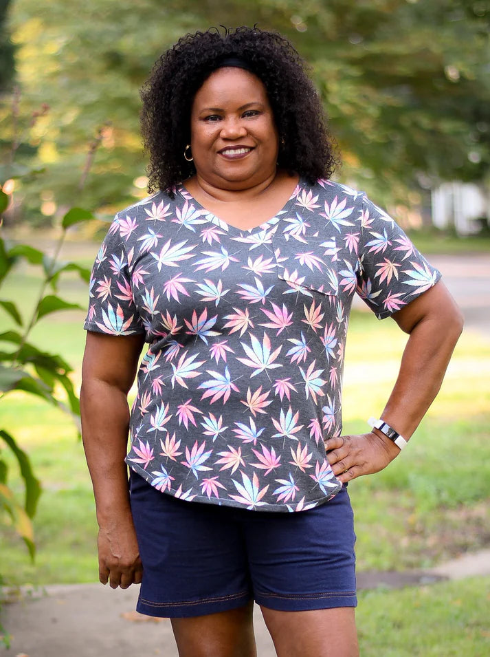 Outdoor view of the Sulky Perfect Tee sewn in a dark knit with a colorful leaf print, paired with dark shorts on a tree‑lined path