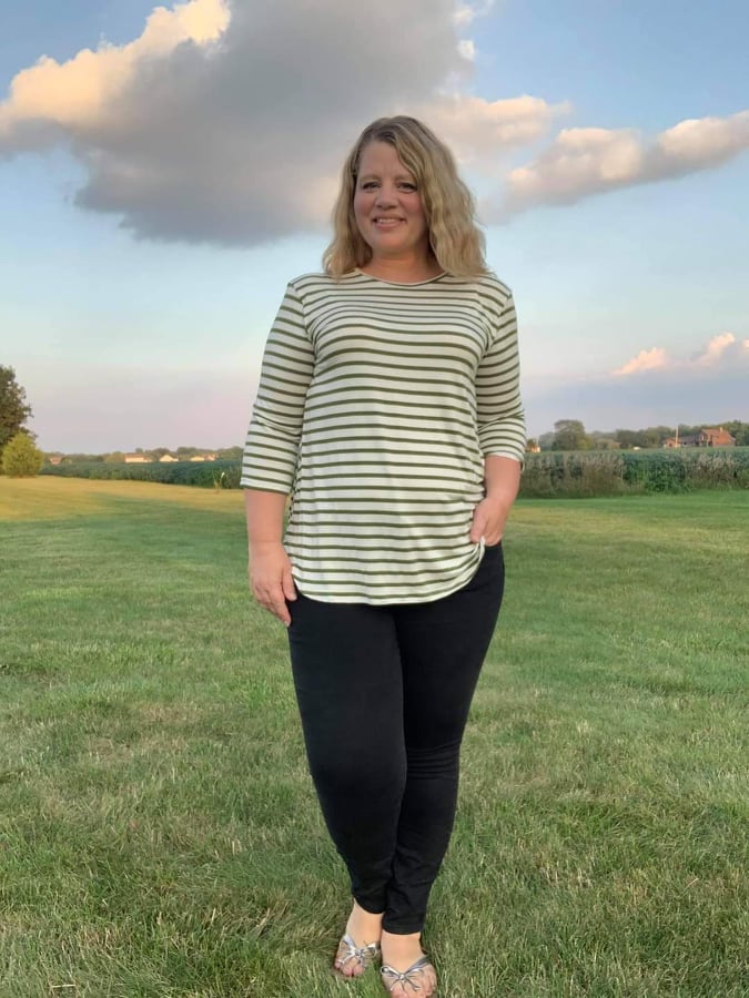 Outdoor view of the Sulky Perfect Tee sewn in a light striped knit with three‑quarter sleeves, worn with black pants in a wide grassy field at sunset