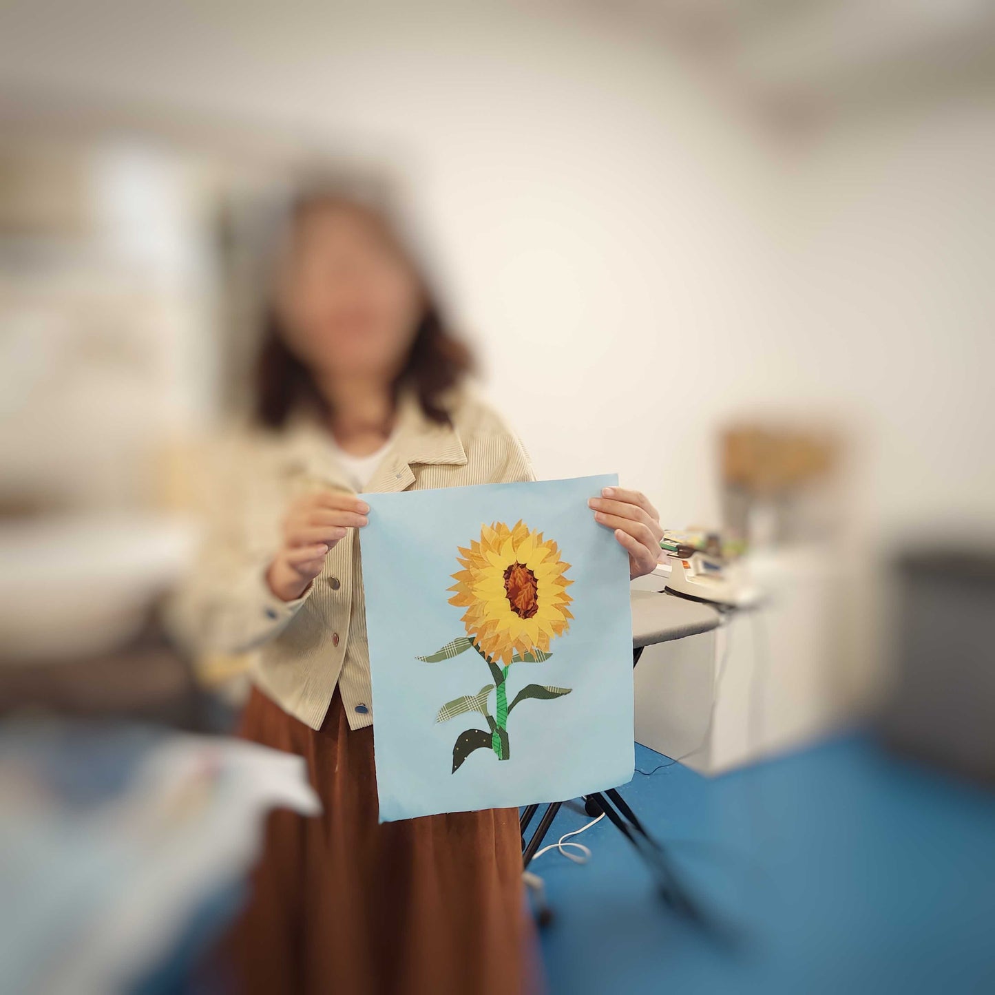 Student holding up a completed sunflower fabric collage block, with background softly blurred.