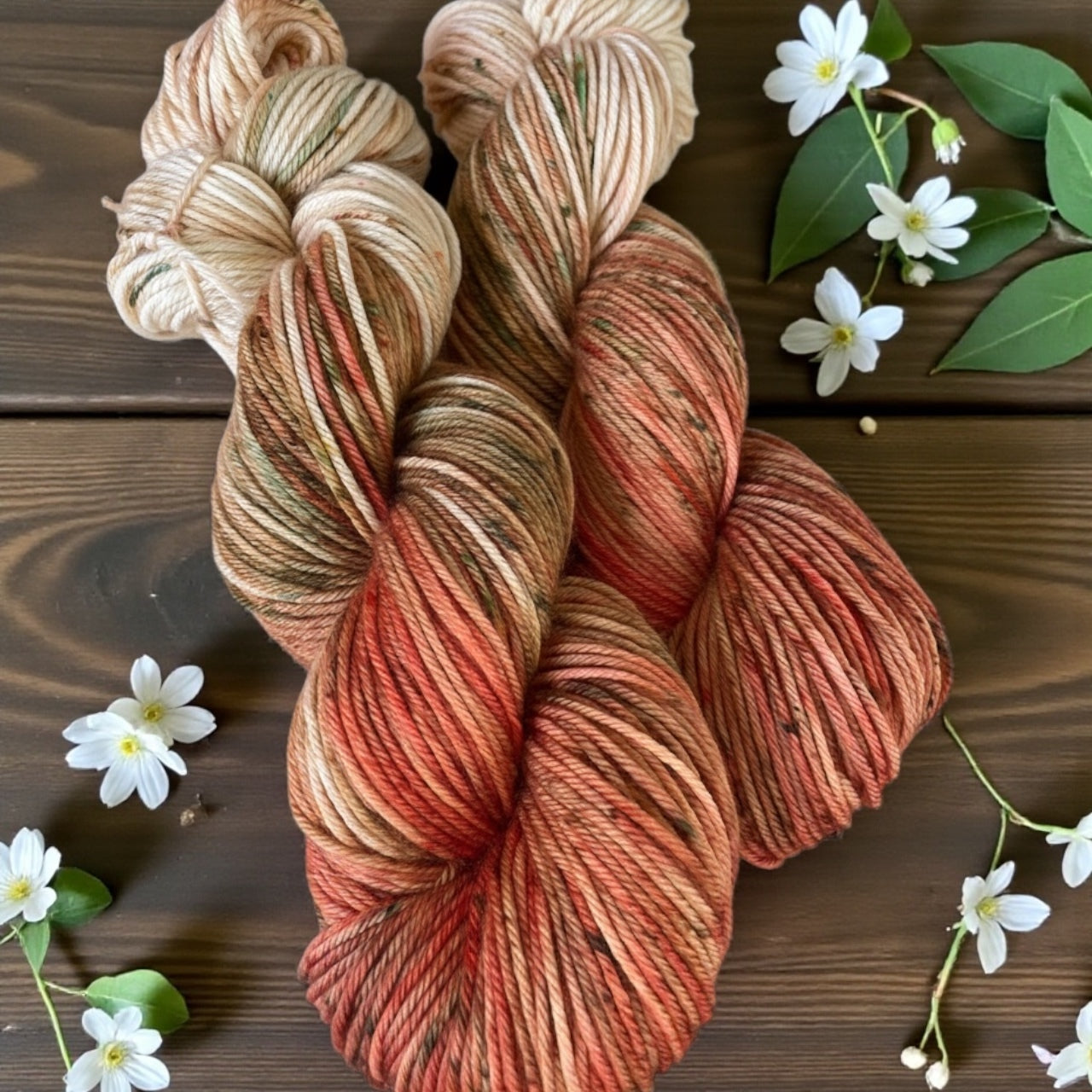 Hand‑dyed yarn in warm peach, coral, and neutral tones with small white flowers.