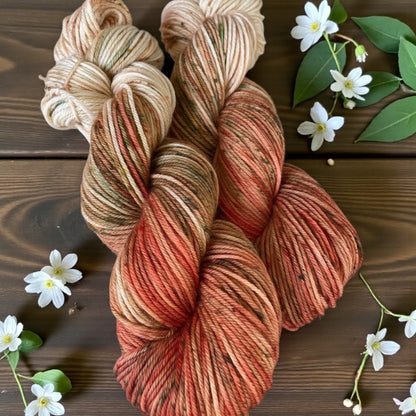 Hand‑dyed yarn in warm peach, coral, and neutral tones with small white flowers.