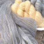 Hand-dyed DK mohair fluff in soft gray and pale yellow tones.
