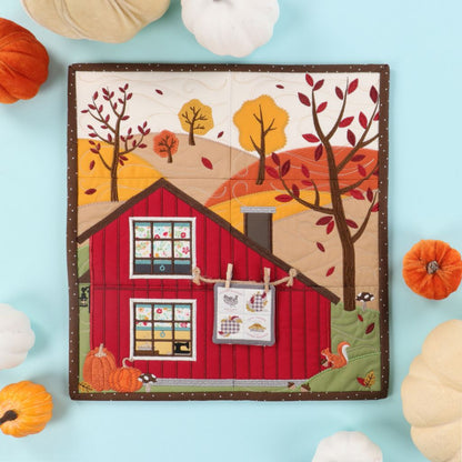 Quilt with a red barn design surrounded by pumpkins on a light blue background